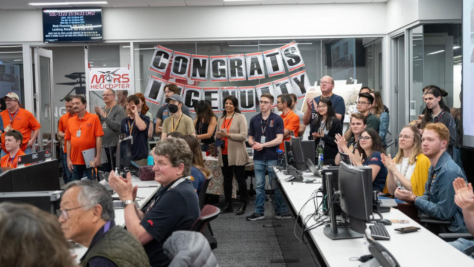 a group of people in an office, some sitting and some standing, applaud.