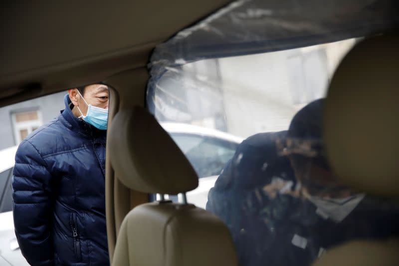 Driver wearing a face mask looks on as a staff member installs plastic shield inside a vehicle at a service centre of car-hailing service Didi Chuxing in Beijing