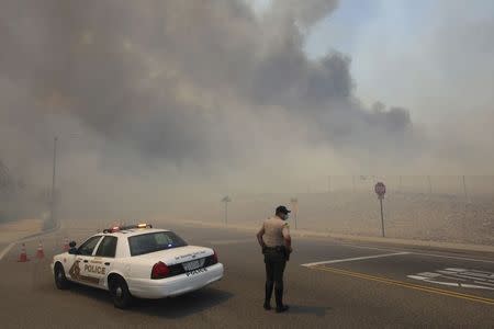 A police officer mans a roadblock as smoke billows from a wildfire driven by fierce Santa Ana winds in Rancho Cucamonga, California April 30, 2014. REUTERS/David McNew