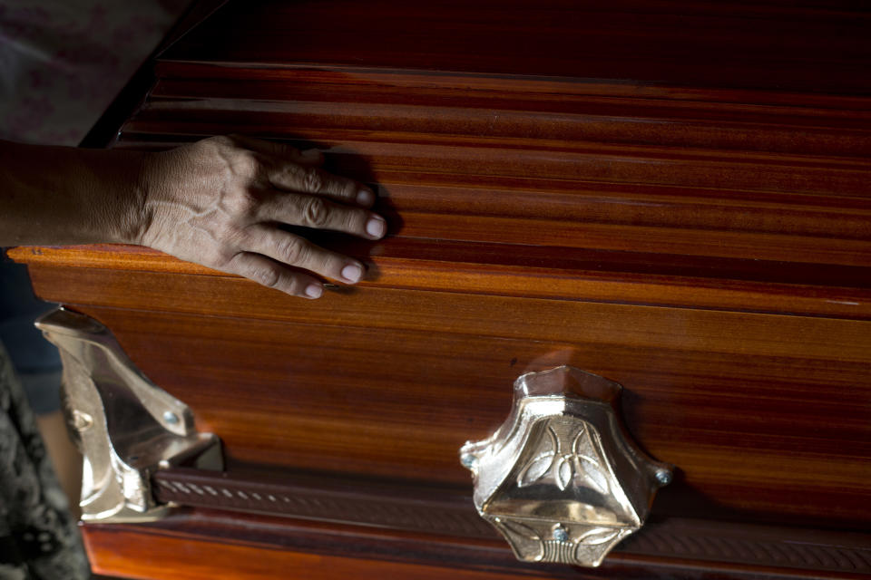 In this Oct. 31, 2018 photo, a woman touches the coffin containing the remains of Wilmer Gerardo Nunez at the end of a wake inside his mother's home in the Cuidad Planeta neighborhood of San Pedro Sula, Honduras. After an eight-year wait, family and friends were able to pay their final respects for Nunez, who went missing when he left for the fourth time to the United States in July of 2010. (AP Photo/Moises Castillo)