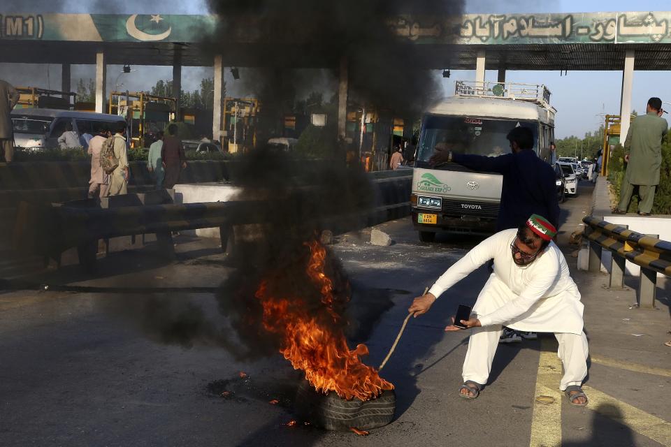 A supporter of former Prime Minister Imran Khan's party burns a tire to block a road during a protest to condemn the election commission's decision, in Islamabad, Pakistan, Friday, Oct. 21, 2022. Pakistan’s elections commission on Friday disqualified former Prime Minister Imran Khan from holding public office for five years, after finding he had unlawfully sold state gifts and concealed assets as premier, officials said. (AP Photo)