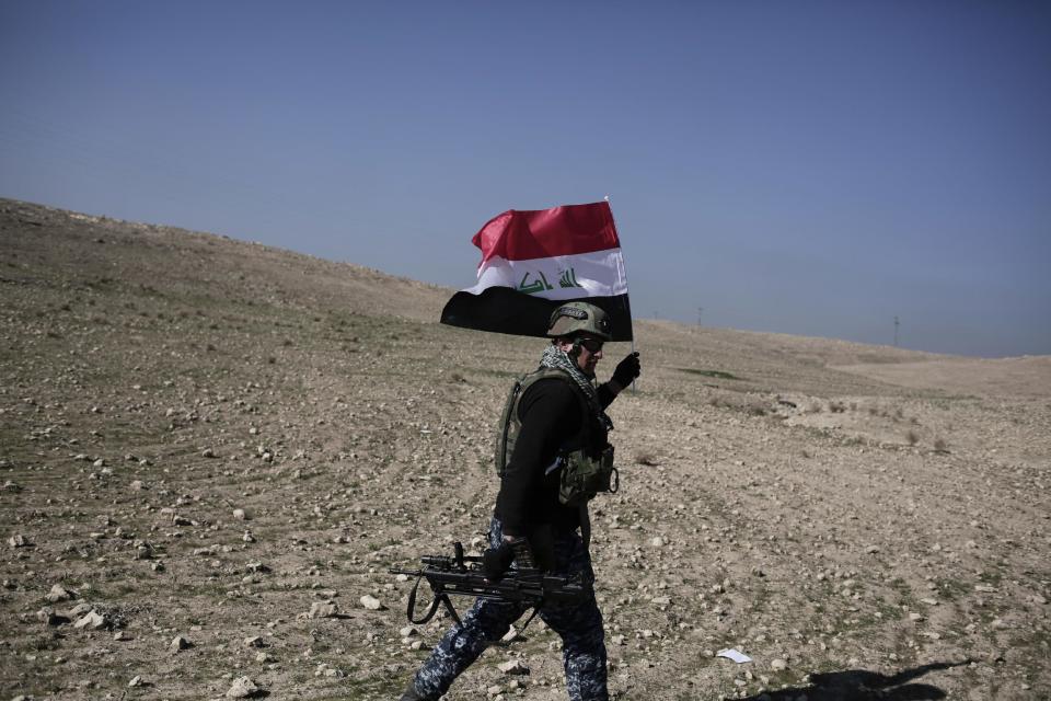 A member of the Iraqi federal police carries an Iraqi flag during a battle against the Islamic State, in Hamam al-Alil, Iraq, Sunday, Feb. 2017. U.S.-backed Iraqi forces launched a large-scale military operation on Sunday to dislodge Islamic State militants from the western half of Mosul city. (AP Photo/Bram Janssen)