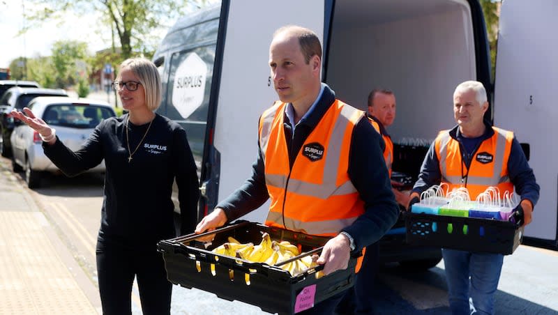 Britain's Prince William, center, carries a crate of bananas as he visits the Hanworth Centre Hub, a youth centre in Feltham, London, Thursday, April 18, 2024. Prince William returned to public duties on Thursday for the first time since his wife’s cancer diagnosis, bolstering the royal family’s ranks as health problems continue to sideline the princess and King Charles III.