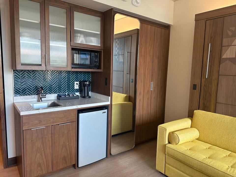 Deluxe studio kitchen in Disneyland resort featuring light wood cabinets, mini fridge, and mirror next to yellow couch