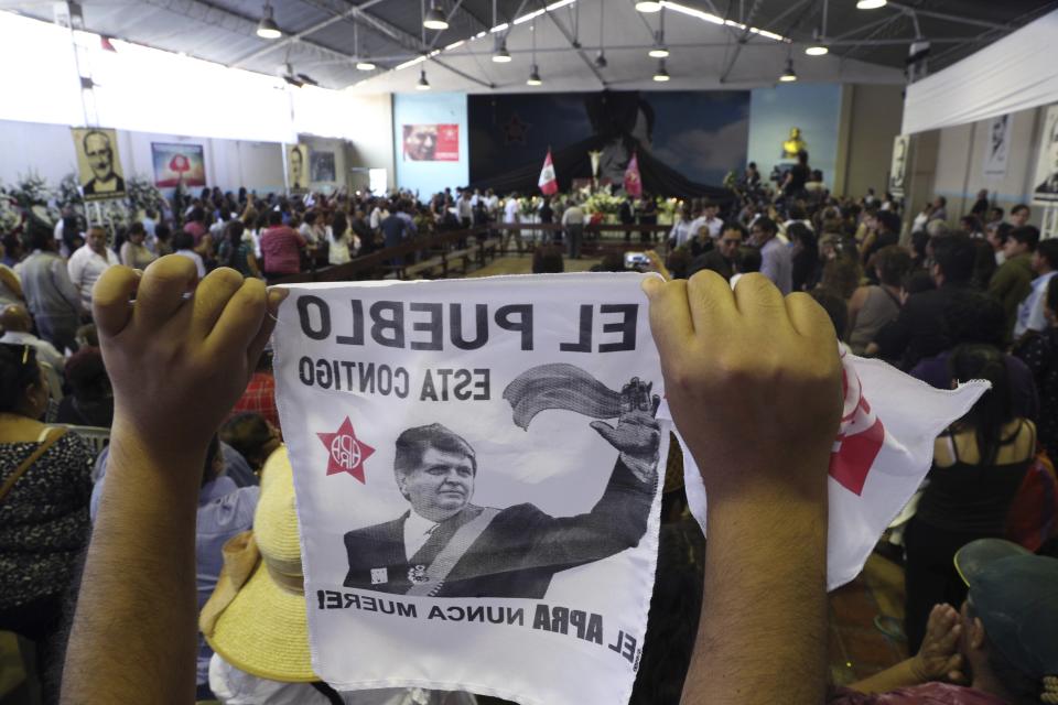 A supporter holds up an image of Peru's late President Alan Garcia on the second day of his wake at his party's headquarters in Lima, Peru, Thursday, April 18, 2019. Garcia shot himself in the head and died Wednesday as officers waited to arrest him in a massive graft probe that has put the country's most prominent politicians behind bars and provoked a reckoning over corruption. (AP Photo/Martin Mejia)