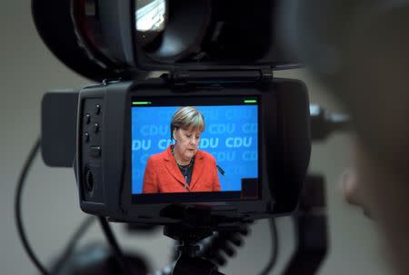 German Chancellor and Christian Democratic Union (CDU) leader Angela Merkel is pictured in a TV camera monitor as she addresses a news conference at CDU party headquarters in Berlin, Germany March 14, 2016. Words read 'The Middle'. REUTERS/Fabrizio Bensch