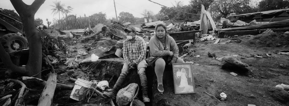 En esta imagen, tomada el 13 de junio de 2018, Marlene Vázquez (derecha) se sienta junto a su primo, Silas Vázquez, con una fotografía de sus primos fallecidos en una erupción del Volcán de Fuego, en San Miguel Los Lotes, Guatemala. El 3 de junio, en un domingo típico, la aldea quedó rápidamente sepultada por una ola de cenizas calientes, piedras y escombros que dejó un paisaje de muerte y desesperación. (AP Foto/Rodrigo Abd)