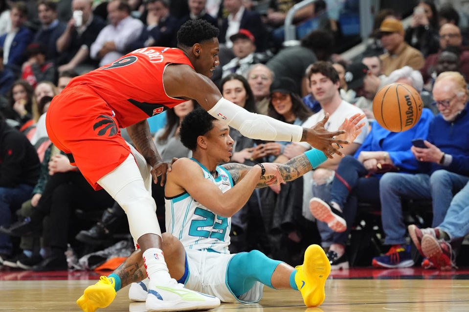 Charlotte Hornets guard Tre Mann (23) plays the ball while sitting on the court as Toronto Raptors guard RJ Barrett (9) defends during first-half NBA basketball game action in Toronto, Sunday, March 3, 2024. (Frank Gunn/The Canadian Press via AP)
