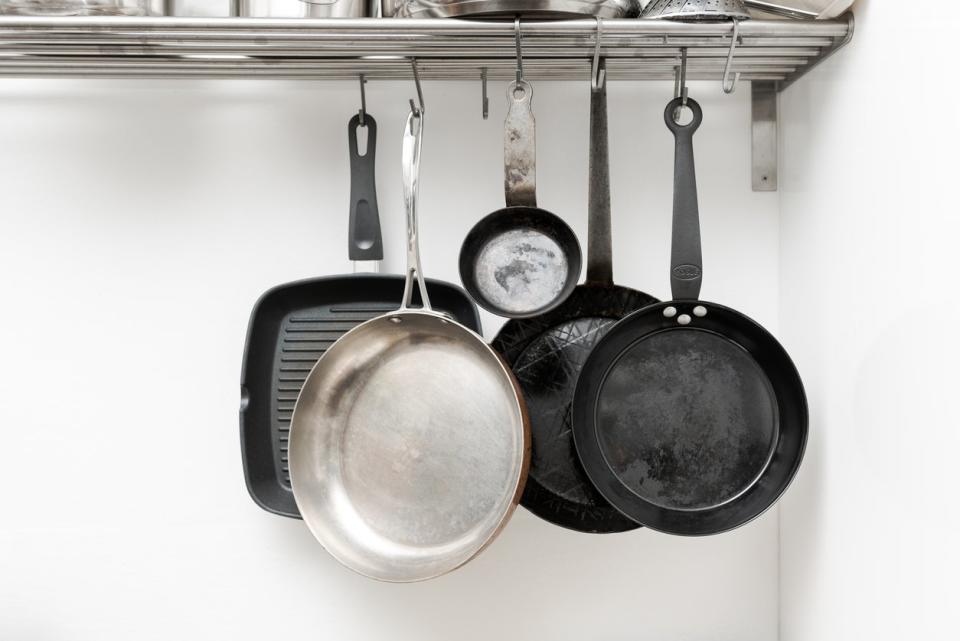 Various pans in different sizes and forms for cooking and frying hanging on metal hooks from shelf in kitchen 