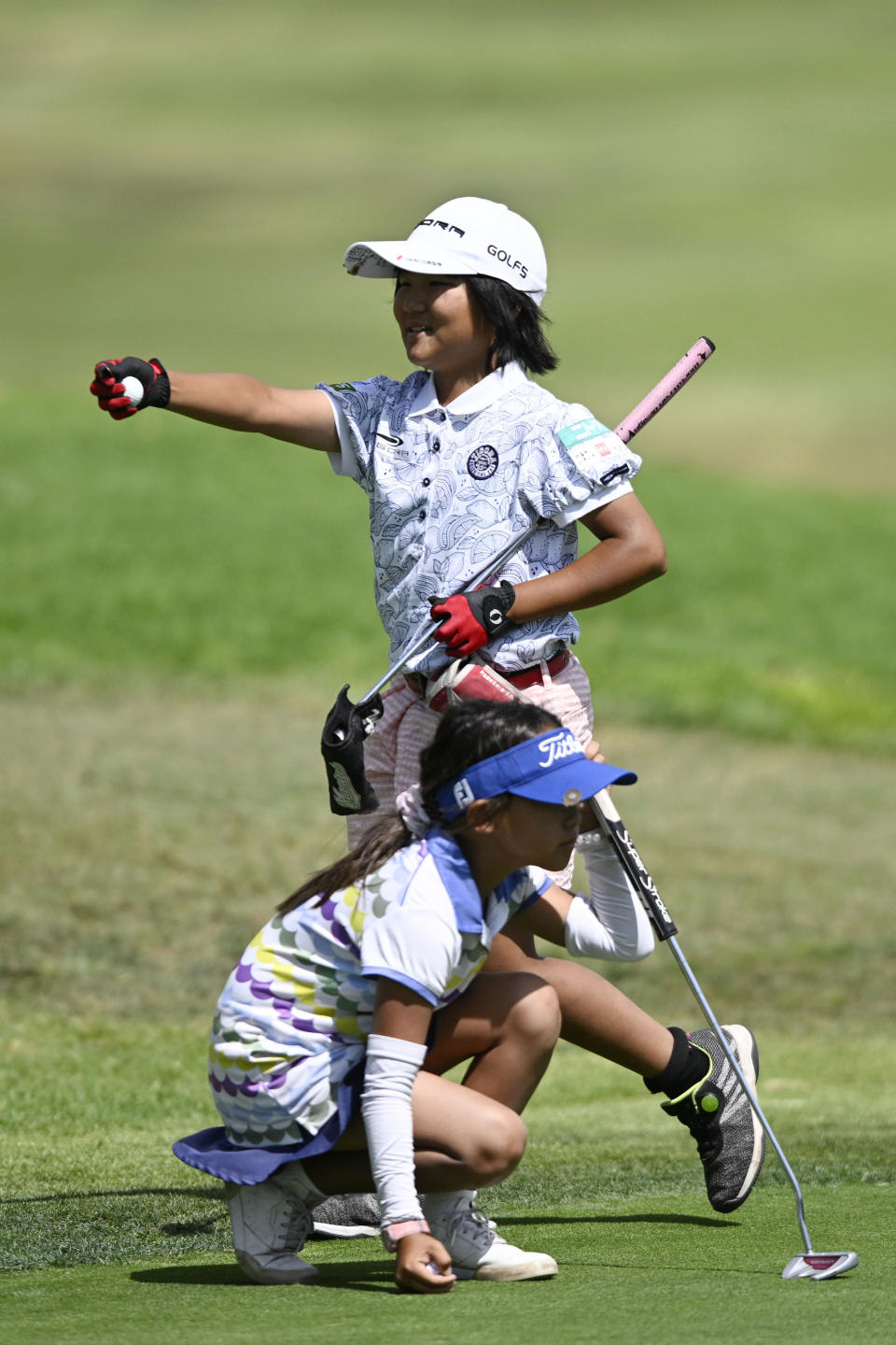 Miroku Suto of Japan holds up the ball after hitting a birdie putt on the ninth hole as Isabell Duan lines up her putt during the final round at the Junior World Championships golf tournament held at Singing Hills Golf Resort on Thursday, July 14, 2022, in El Cajon, Calif. (AP Photo/Denis Poroy)