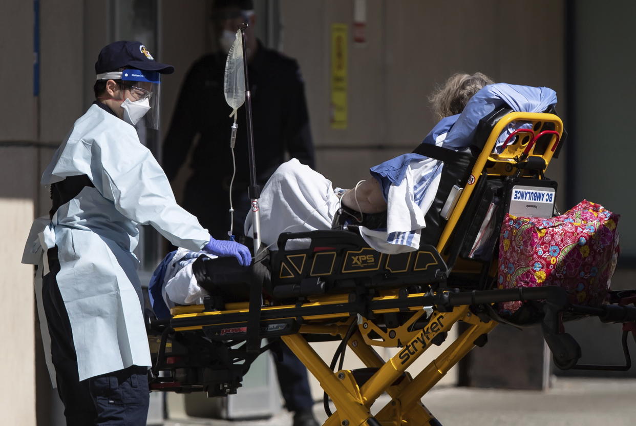 A B.C. Ambulance Service employee in protective equipment including an N95 mask, a face shield, goggles and gloves, moves a patient from an ambulance to the emergency department at Royal Columbian Hospital in New Westminster, British Columbia, on Sunday, April 12, 2020. (Darryl Dyck/The Canadian Press via AP)