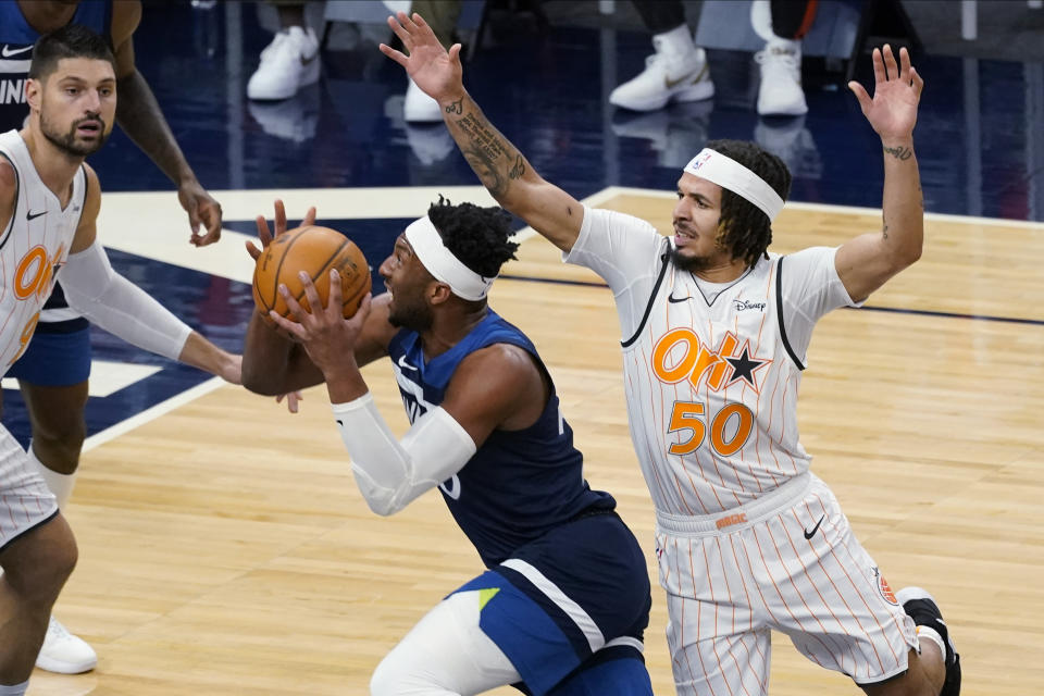 CORRECTS ORLANDO PLAYER AT LEFT TO NIKOLA VUCEVIC, INSTEAD OF AARON GORDON - Minnesota Timberwolves' Josh Okogie, center, drives between Orlando Magic's Cole Anthony, right, and Nikola Vucevic during the first half of an NBA basketball game Wednesday, Jan. 20, 2021, in Minneapolis. (AP Photo/Jim Mone)