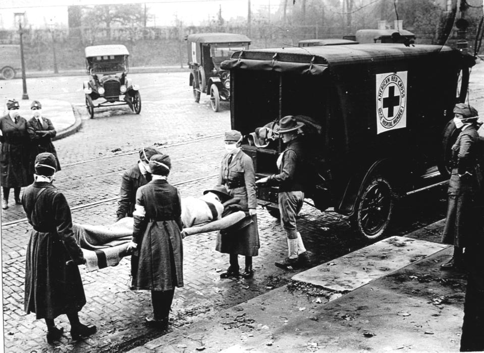 Members of the Red Cross Motor Corps, all wearing masks against the further spread of the influenza epidemic, carry a patient on a stretcher into their ambulance, Saint Louis, Missouri, October 1918. (Photo by PhotoQuest/Getty Images)