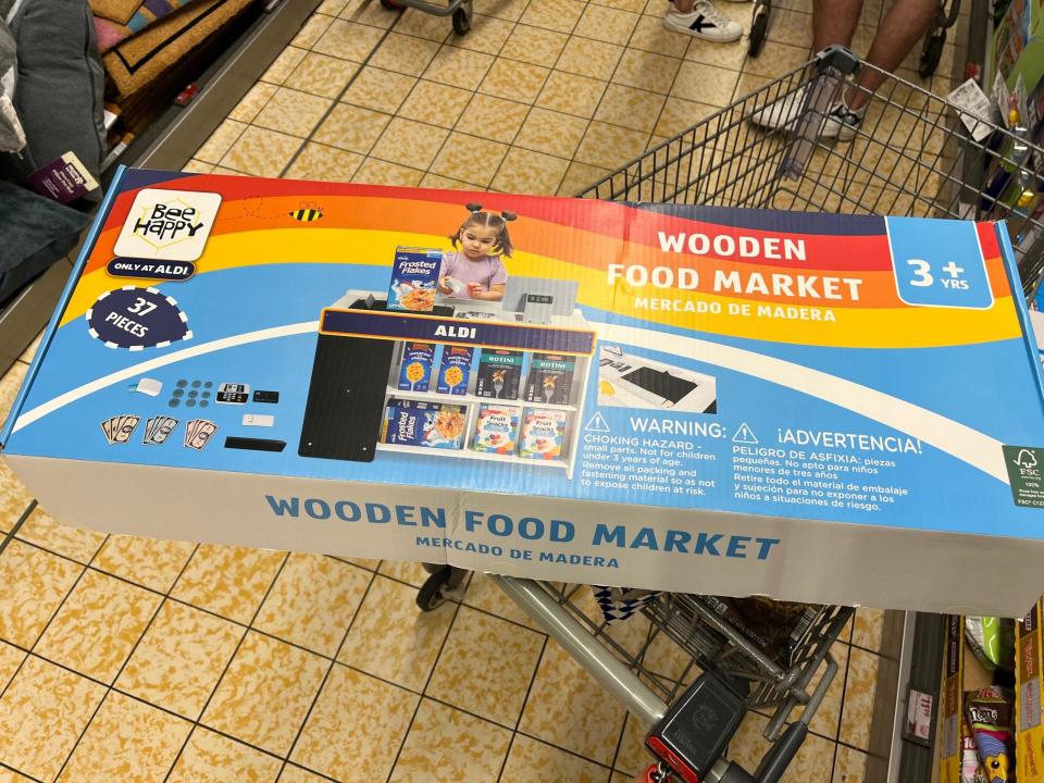 Ein Aldi-Spielset "Wooden Food Market" für Kinder steht auf einem Einkaufswagen in einem Aldi-Markt in Maryland. Auf der Verpackung ist das Foto eines Kindes abgebildet, das mit dem Set einkaufen geht. Dazu gehören ein Spielzeugkassenständer, Spielgeld und Pappschachteln, die Aldi-Produkte nachahmen.