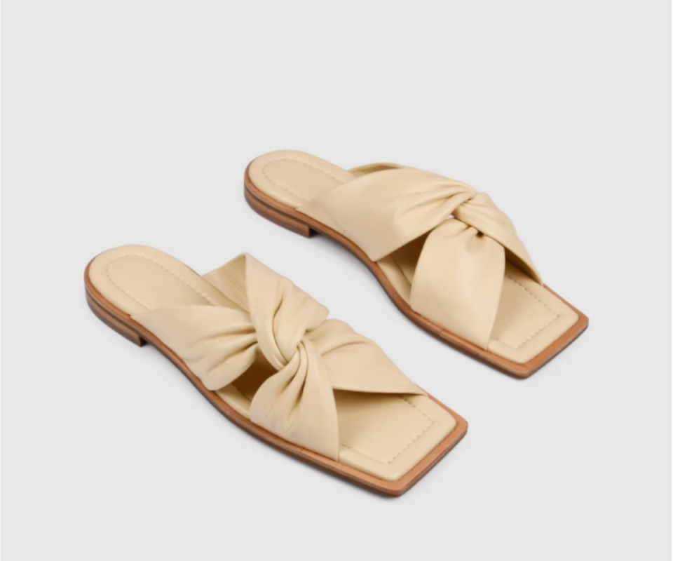 A pair of beige leather twist sandals on a white background.