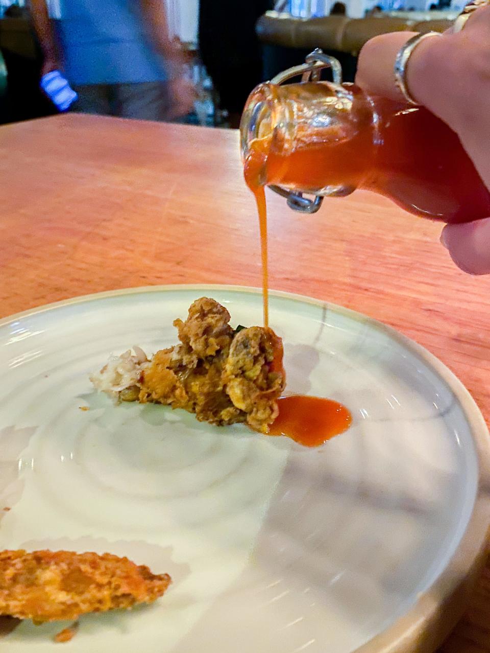 The author pours hot honey sauce on the fried chicken