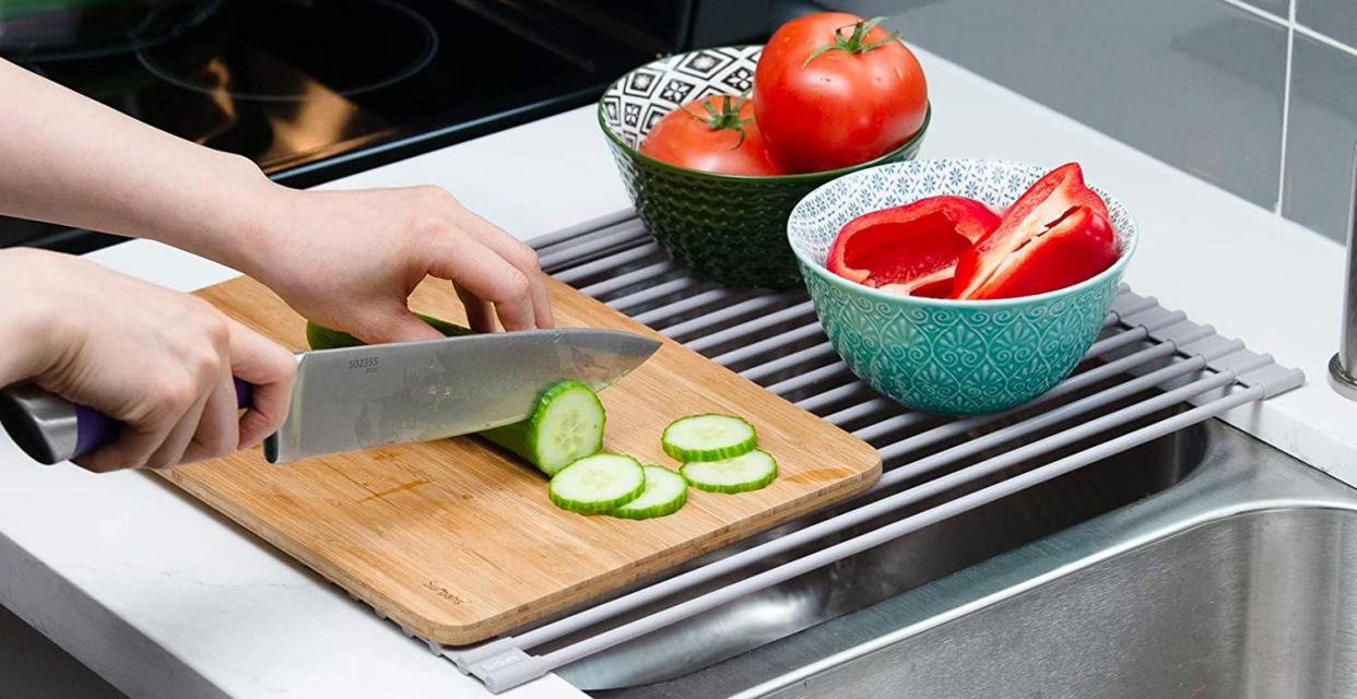 dish rack with dishes of fruits and vegetables and a person cutting cucumbers on a cutting board on the rack 