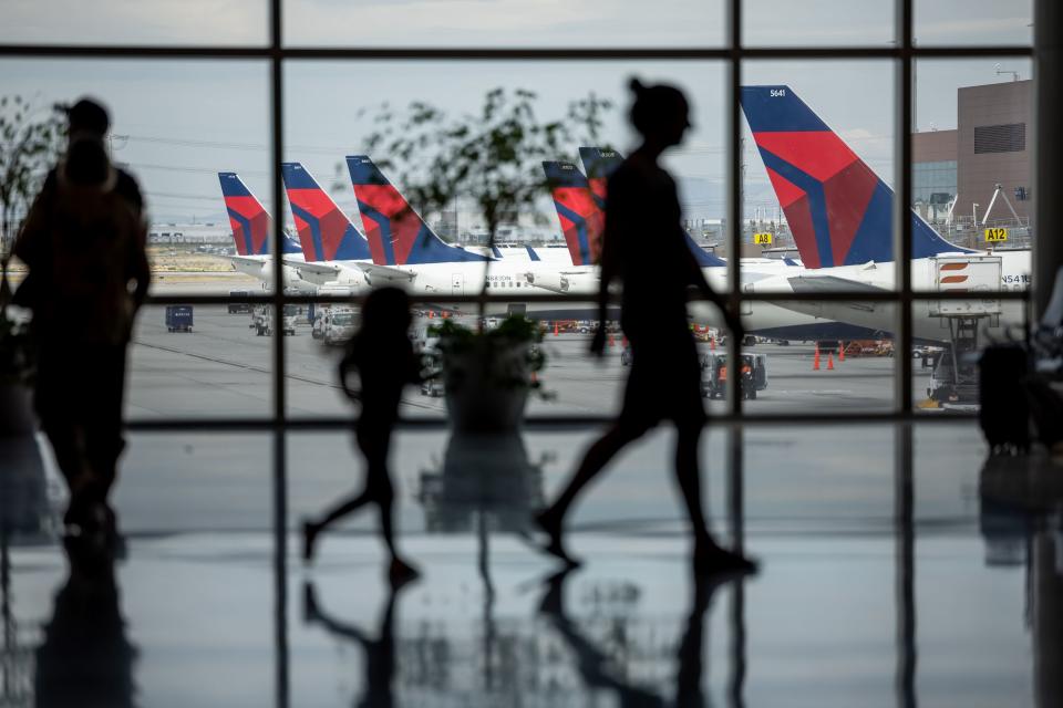 People walk through the baggage claim with Delta jets visible at their gates at the Salt Lake City International Airport.