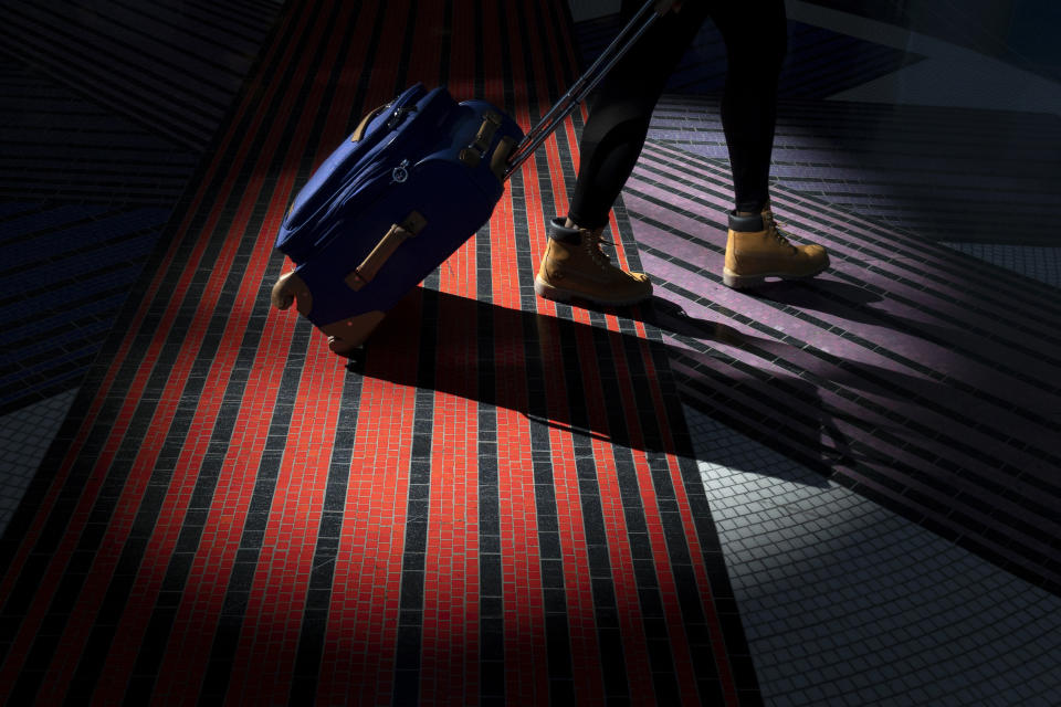 FILE - In this Nov. 21, 2018, file photo a traveler walks with a suitcase through the terminal at Washington Reagan National Airport in Arlington, Va. More than 7 in 10 U.S. airline passengers (72%) say ticket price is a key deciding factor when choosing an airport to fly into or from, according to a 2019 survey commissioned by NerdWallet and conducted online by The Harris Poll among more than 1,800 U.S. adults who have ever flown on an airplane. (AP Photo/Carolyn Kaster, File)