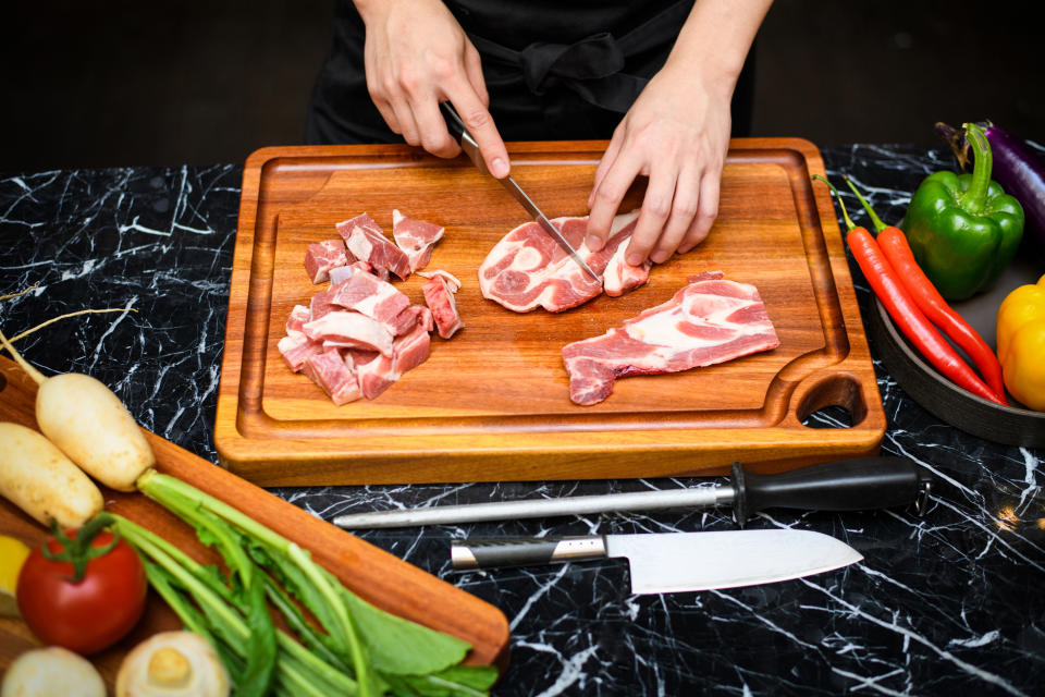 person cutting raw meat on a cutting board with raw vegetables nearby