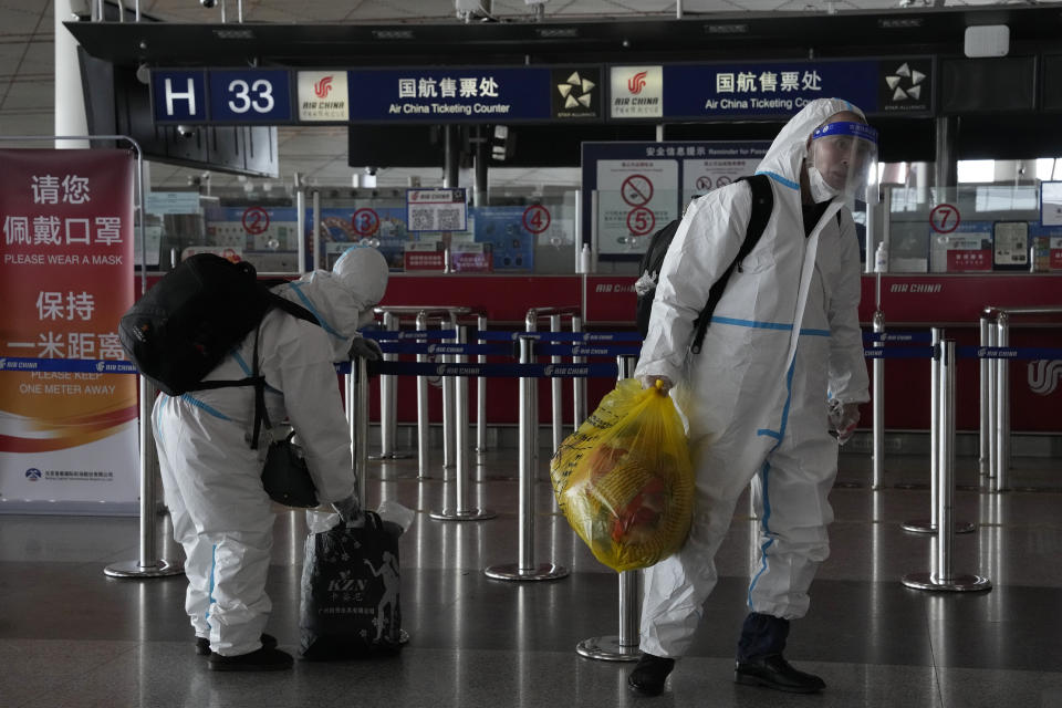 Passengers in protective gear carry their luggage in the Capital airport terminal in Beijing, Tuesday, Dec. 13, 2022. Some Chinese universities say they will allow students to finish the semester from home in hopes of reducing the potential of a bigger COVID-19 outbreak during the January Lunar New Year travel rush. (AP Photo/Ng Han Guan)