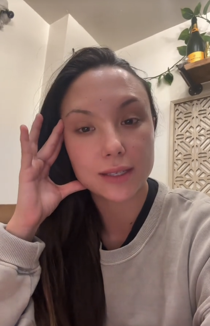 Allie resting her face on her hand, with a ponytail and a casual top, indoors