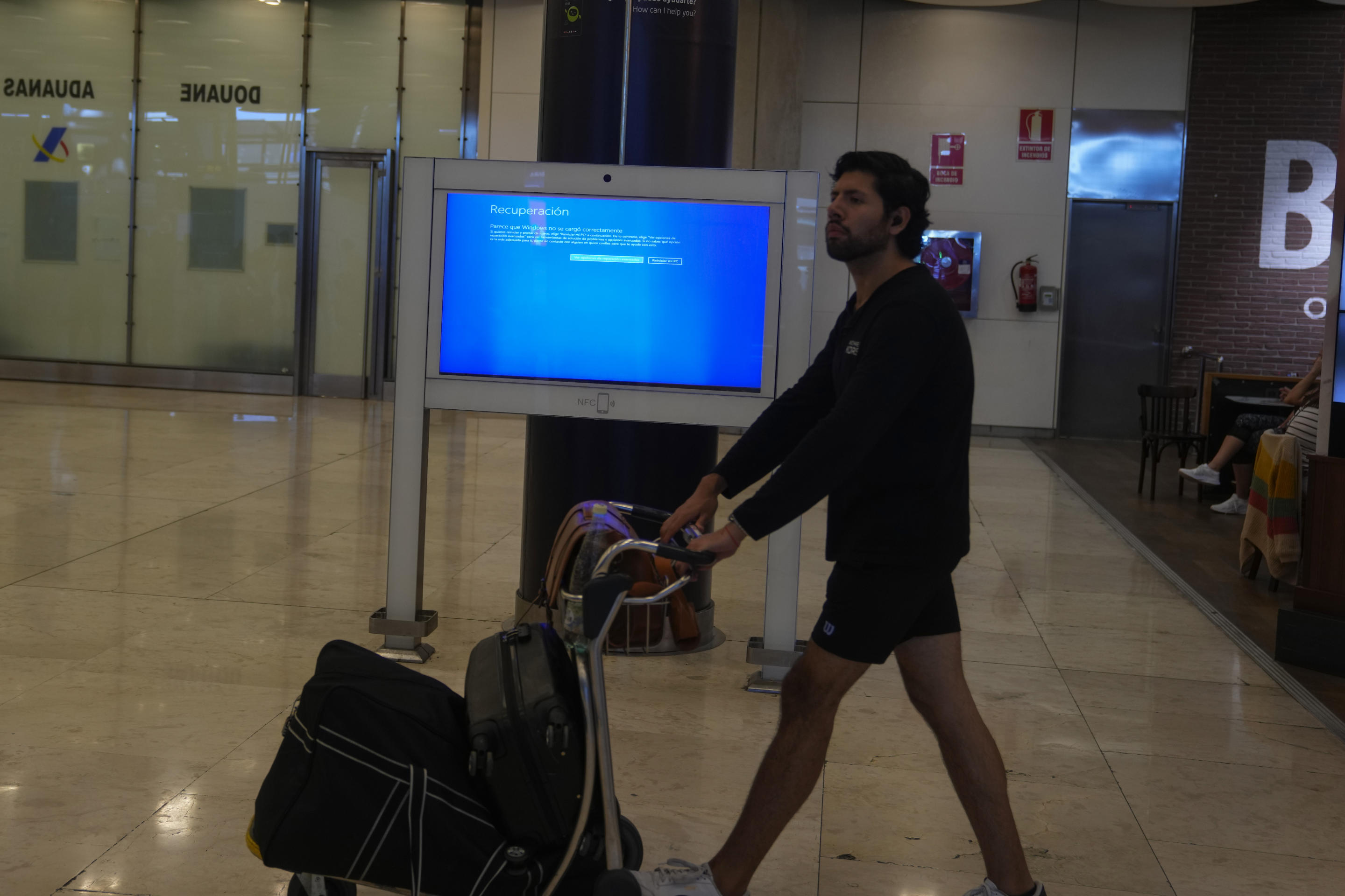 A screen displays a Microsoft Windows recovery message at Madrid airport.