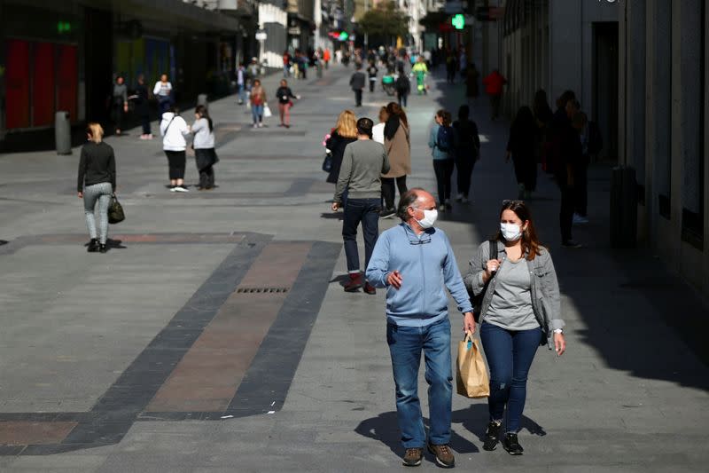 A couple wear protective masks as they walk in unusually quiet Preciados street in Madrid