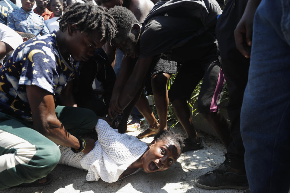 During a funeral for two people killed in violence related to recent protests, mourners restrain a woman related to one of the victims after she went into a trance at Champ de Mars park near the National Palace in Port-au-Prince, Haiti, Wednesday, Oct. 16, 2019. Funerals for 11 of at least 20 people killed were held in six cities, including the capital of Port-au-Prince, where at least two people were injured in a protest that broke out when presidential guards tried to block a road near where hundreds had gathered around the coffins of two victims. (AP Photo/Rebecca Blackwell)