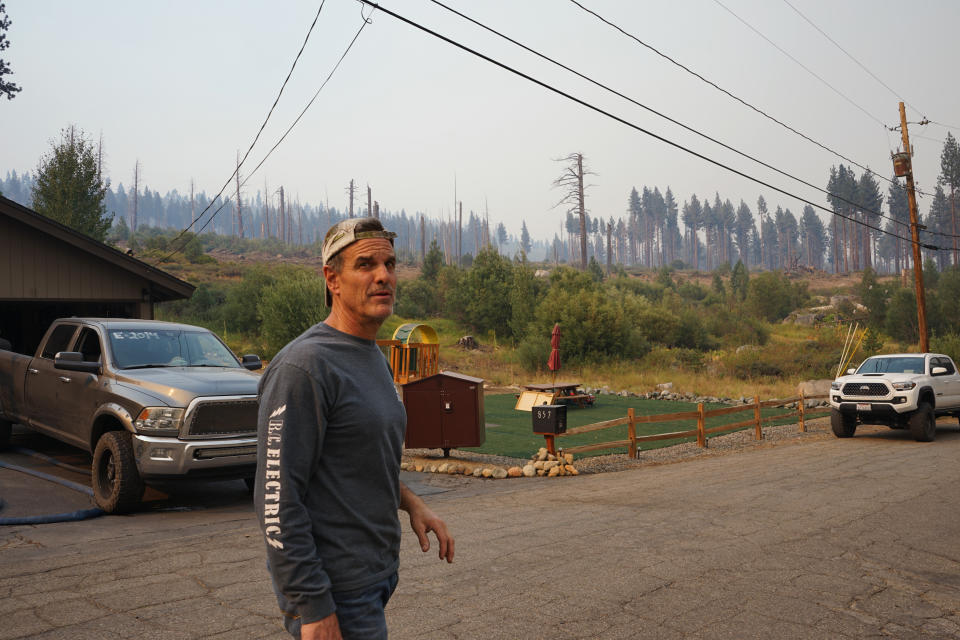 John Rhodes stands Tuesday, Aug. 31, 2021, in his Meyers, Calif., neighborhood in front of charred trees burned by the 2007 Angora Fire. Rhodes and four neighbors chose to remain in the South Lake Tahoe area in defiance of the evacuation order issued Monday in order to defend their homes from encroaching flames. The group, who included off-duty firefighters, used hoses and hydrant water to create a perimeter around the neighborhood and ventured to the fire line in Christmas Valley to see if firefighters needed assistance. (AP Photo/Sam Metz)