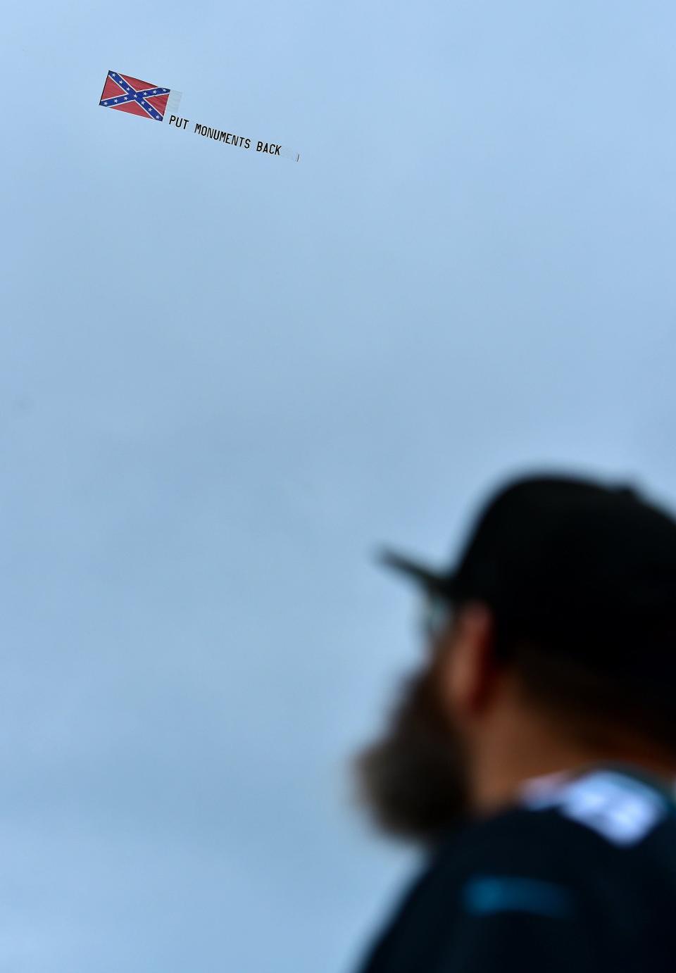 A spectator at Sunday's NFL game between the Baltimore Ravens and the Jacksonville Jaguars watches a plane pull a banner saying "Put Monuments Back" and flying a Confederate flag circle TIAA Bank Field.