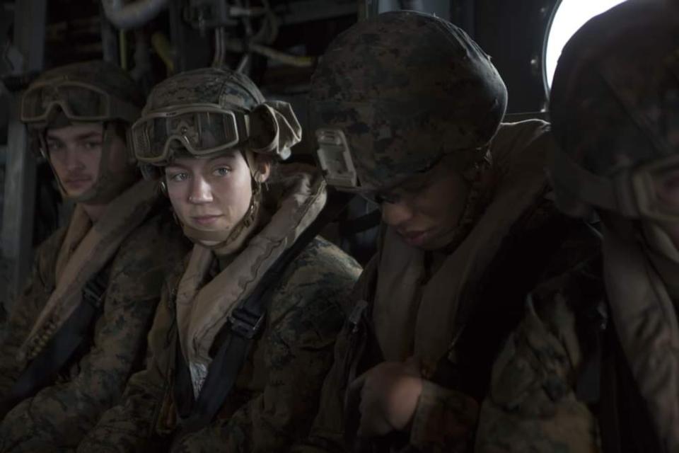 Marines sit a row. One of their faces is illuminated