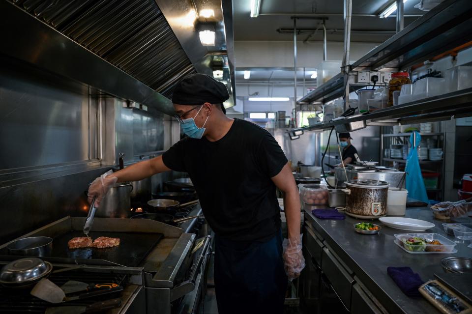 <p>Uno de los cocineros prepara los platos que los clientes van a disfrutar en sus vehículos. (Photo by MOHD RASFAN/AFP via Getty Images)</p> 