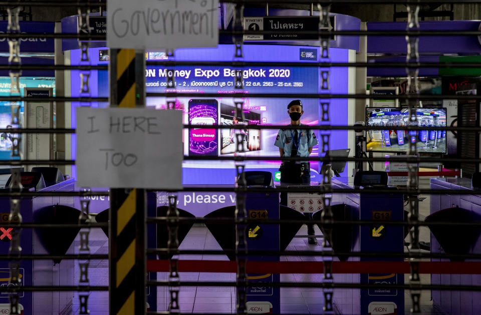 A security guard stands watch as placards against shutting down mass transport systems hang at Ashok BTS station in Bangkok, Thailand, Sunday, Oct. 18, 2020. The authorities in Bangkok on Sunday shut down a mass transit line as Thailand's capital city braced for a fifth straight day of determined anti-government protests. (AP Photo/Gemunu Amarasinghe)