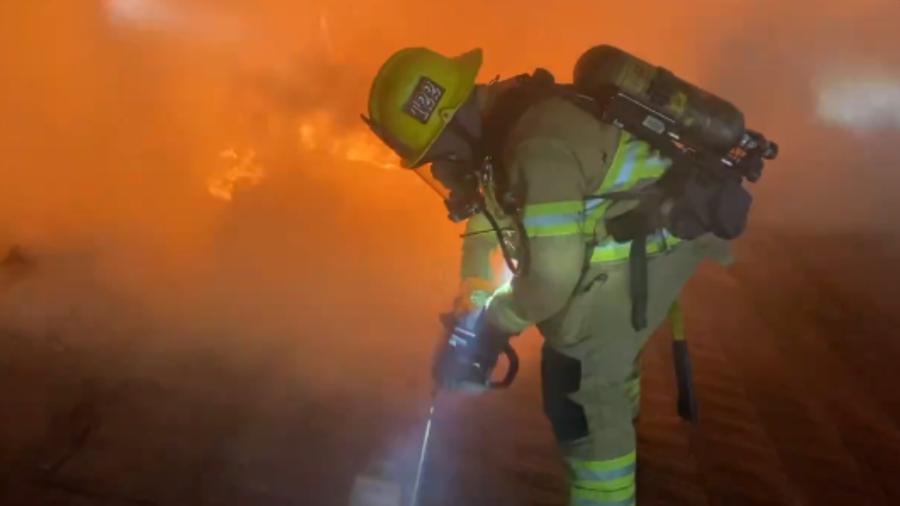 Firefighter cuts through the roof of a burning home in Laguna Woods