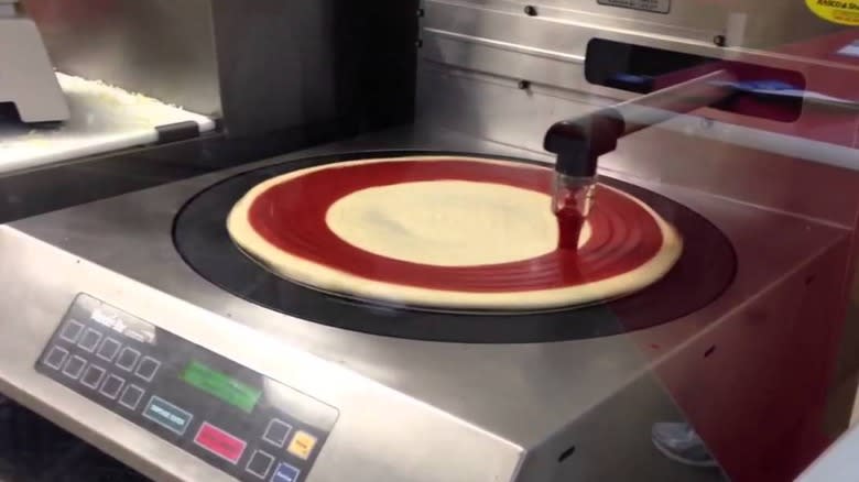 A pump dispenses tomato sauce onto pizza dough