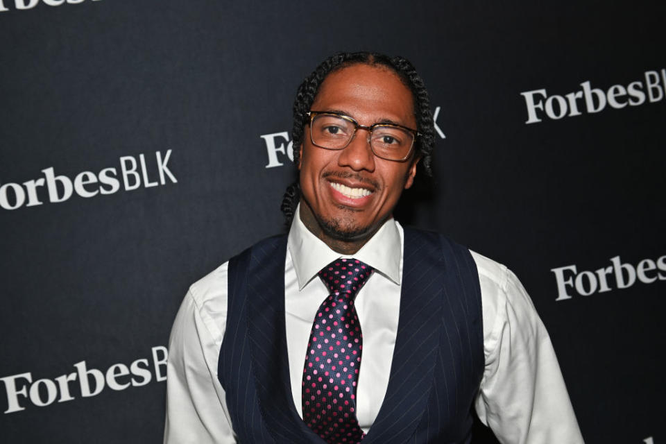 Nick Cannon attends a ForbesBLK event wearing a pinstriped vest, white dress shirt, and polka-dot tie, smiling for the camera