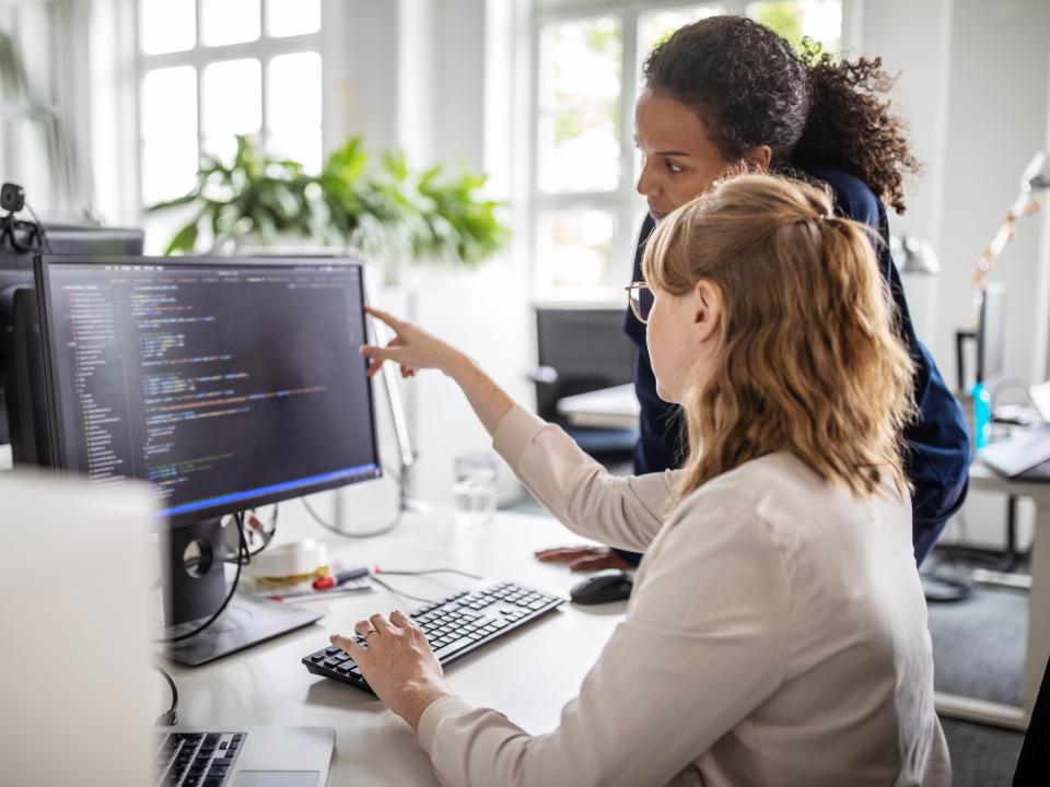 Businesswoman discussing computer program with female colleague at desk in creative office