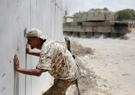 A fighter of Libyan forces allied with the U.N.-backed government looks through a hole in a wall as a self-propelled artillery gun fires at Islamic State fighters during a battle in Sirte, Libya. REUTERS/Goran Tomasevic