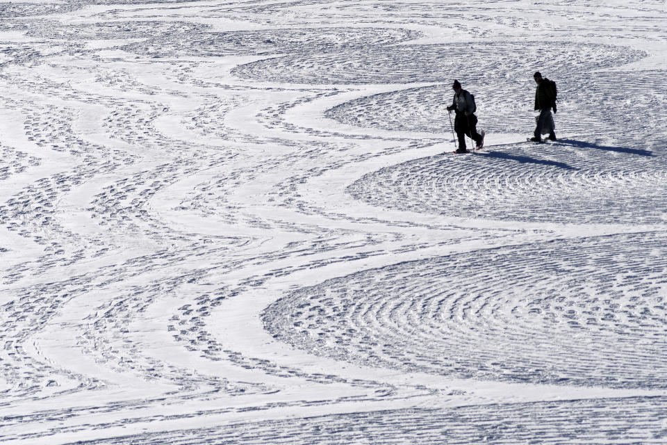 In this photo taken Jan. 7, 2020, British artist Simon Beck, left, and a volunteer put the final touches on a geometrical snow drawing on a frozen reservoir near Silverthorne, Colo. Beck says he hopes his art makes people more aware of the beauty of the environment. (AP Photo/Thomas Peipert)