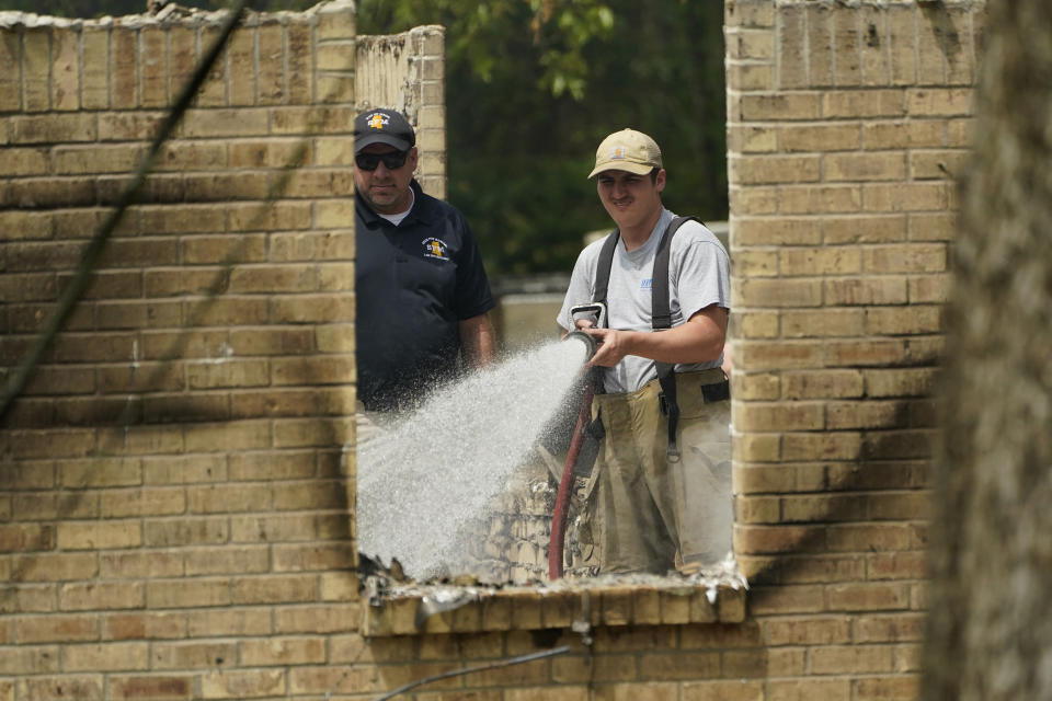 A member of the Mississippi State Fire Marshal's Office, left, waits as a firefighter waters down hot spots inside a burned out house, Wednesday morning, April 26, 2023, in Conway, Miss. Authorities believe a man who escaped from a Mississippi jail over the weekend with three others, and is suspected of killing a pastor, is believed to be dead in the house after a shootout with authorities and barricaded himself inside a burning home near Conway, Mississippi. (AP Photo/Rogelio V. Solis)