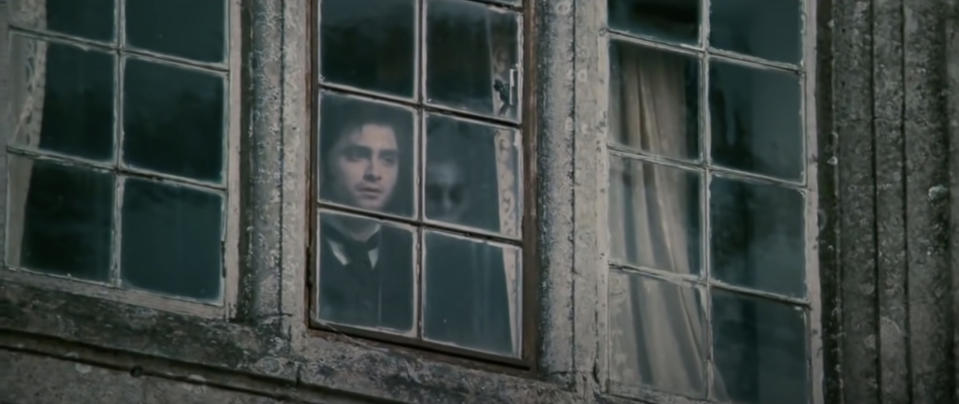 Man stands in the window with a scary face looming behind him