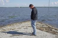 In this May 10, 2019 photo, Brett Adams stands where the road to his flooded farm disappears under flood waters, with the farm buildings visible in the background, in Peru, Neb. Adams had thousands of acres under water, about 80 percent of his land, this year. The water split open his grain bins and submerged his parents' house and other buildings when the levee protecting the farm broke. (AP Photo/Nati Harnik)