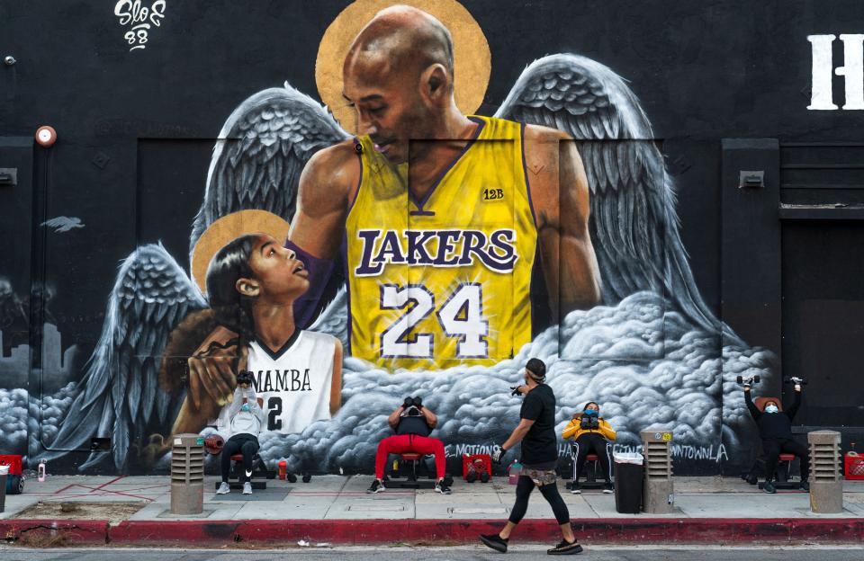 People lift weights on a sidewalk outside the Hardcore Fitness gym, due to COVID-19 restrictions, under a mural honoring NBA star Kobe Bryant and his daughter Gigi near Staples Center in downtown Los Angeles on Jan. 25, 2021.