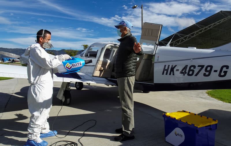 A man using protective gear disinfects a passenger before boarding a plane that collects samples of the corovirus disease (COVID-19) in villages with difficult access, in Bogota