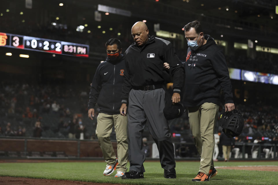 Home plate umpire Kerwin Danley, center, is helped off the field by Anthony Reyes, left, and Dave Groeschner after being knocked down by a ball during the sixth inning at the Colorado Rockies and San Francisco Giants baseball game in San Francisco, Tuesday, April 27, 2021. (AP Photo/Jed Jacobsohn)