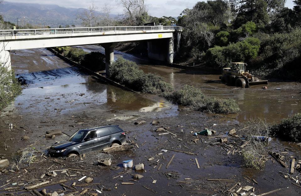 FILE - A bulldozer moves debris as a vehicle sits stranded in flooded water on U.S. Highway 101 in Montecito, Calif., Jan. 10, 2018. Experts say California has learned important lessons from the Montecito tragedy, and the state has more tools to pinpoint the hot spots and more basins and nets are in place to capture the falling debris before it hits homes. (AP Photo/Marcio Jose Sanchez, File)