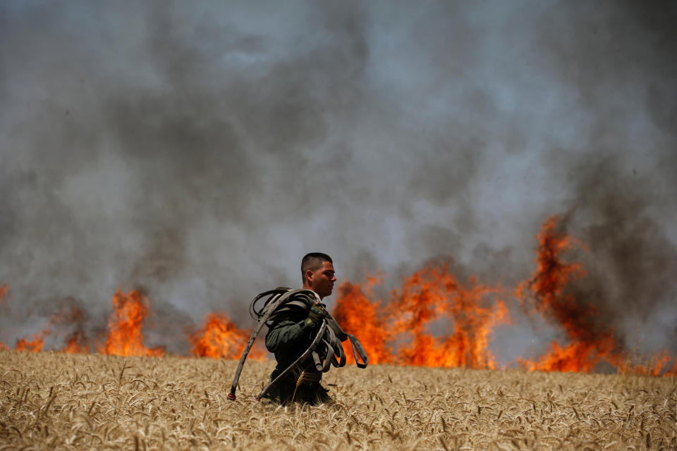 An Israeli soldier carries a hose as he walks in a burning field on the Israeli side of the border fence between Israel and Gaza.&nbsp;