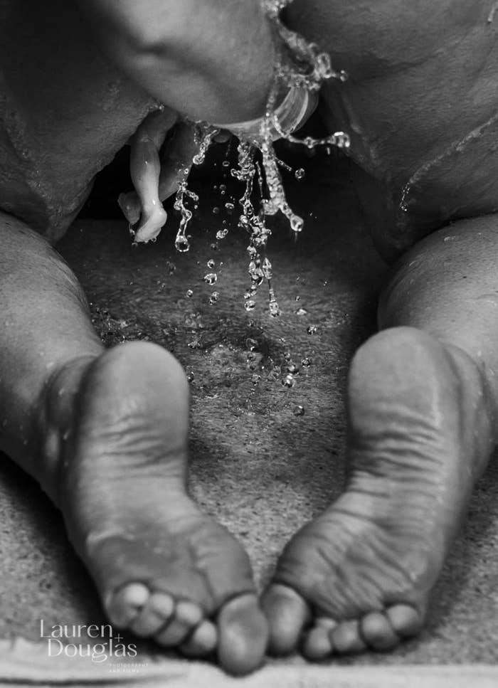 A woman is on her hands and knees as the tiny feet of a baby hang out of her body