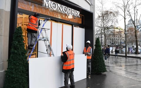 People are at work to build a wooden wall aimed at protecting the shop window of supermarket, on the Champs-Elysees in Paris - Credit: AFP